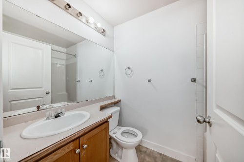 Bathroom featuring a vanity with a white oval sink, chrome faucet, and wood cabinetry, alongside a toilet and a large wall-mounted mirror - 126 16221 95 Street, Edmonton, AB - Indoor Photo Showing Bathroom