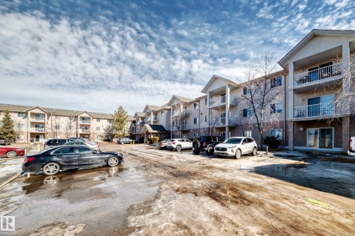 The property features a multi-story building with balconies, a paved parking area, and visible trees - 126 16221 95 Street, Edmonton, AB - Outdoor With Facade