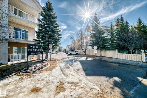 The property features a multi-story building with balconies, set along a paved road with surrounding trees and a fence - 126 16221 95 Street, Edmonton, AB - Outdoor