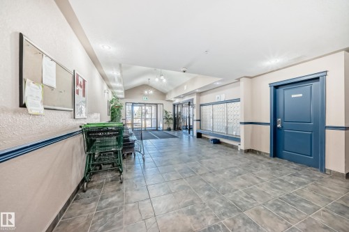 The property features a spacious hallway with tile flooring, a blue door, and large windows at the end of the hall - 126 16221 95 Street, Edmonton, AB - Indoor Photo Showing Other Room