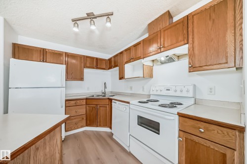 The kitchen features wooden cabinetry, white appliances, and light-colored countertops - 126 16221 95 Street, Edmonton, AB - Indoor Photo Showing Kitchen With Double Sink