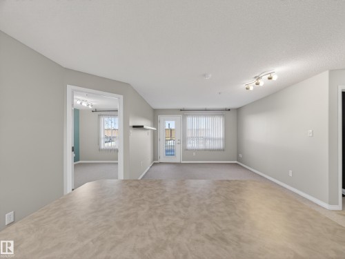 The property features light-colored walls and carpeting, a window with blinds, and track lighting - 1111 9363 Simpson Drive, Edmonton, AB - Indoor Photo Showing Other Room