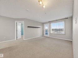 Spacious living area featuring neutral carpeting, a large window with vertical blinds, and access to an exterior balcony - 