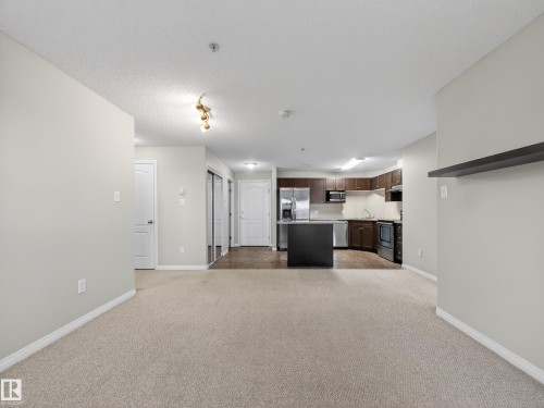 Open concept living space featuring neutral-toned carpeting, a modern kitchen with dark wood cabinetry and stainless steel appliances, and a central kitchen island - 1111 9363 Simpson Drive, Edmonton, AB - Indoor