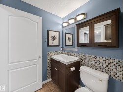 Well-appointed bathroom featuring a dark wood vanity with white basin, mosaic tile backsplash, and a wall-mounted mirrored medicine cabinet - 