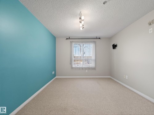 The room features carpeted flooring, a window with vertical blinds, and a light fixture with four bulbs - 1111 9363 Simpson Drive, Edmonton, AB - Indoor Photo Showing Other Room