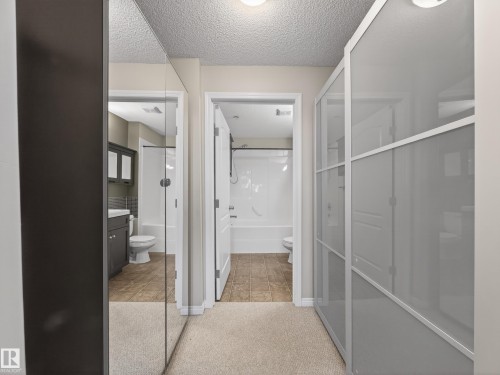 Hallway with carpeted flooring, featuring a mirrored closet door and a second closet with frosted glass panels - 1111 9363 Simpson Drive, Edmonton, AB - Indoor