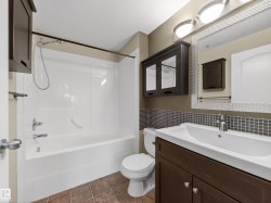 Bathroom featuring a white tub and shower combination, a dark wood vanity with a white sink, and a tiled floor - 