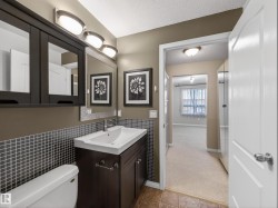 Bathroom featuring a vanity with a white sink and dark cabinetry, a wall-mounted mirror, and a tiled backsplash - 