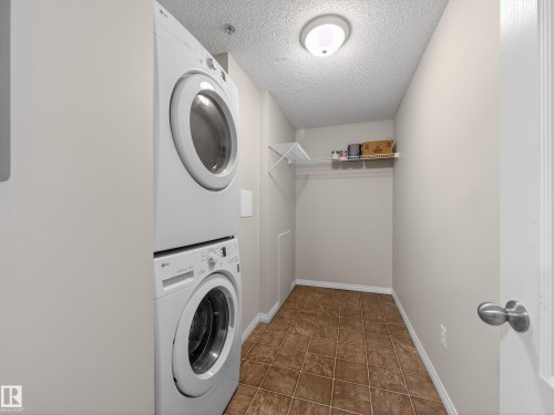 Laundry area featuring a stacked washer and dryer, tile flooring, and a wall-mounted shelf - 1111 9363 Simpson Drive, Edmonton, AB - Indoor Photo Showing Laundry Room