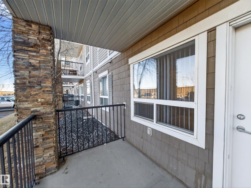 Outdoor patio area with a stone-clad pillar, providing a view of the exterior siding and an adjacent window with vertical blinds - 1111 9363 Simpson Drive, Edmonton, AB - Outdoor With Exterior