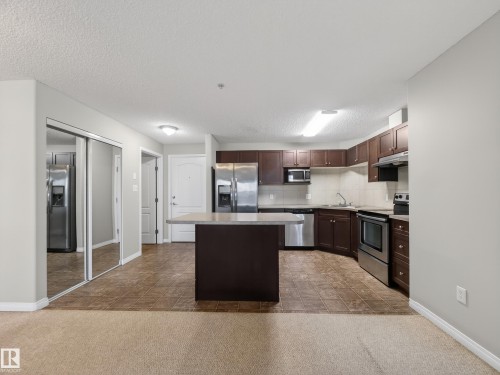 The property features a kitchen with dark wood cabinetry, stainless steel appliances, and a central island with a countertop - 1111 9363 Simpson Drive, Edmonton, AB - Indoor Photo Showing Kitchen With Upgraded Kitchen