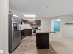 The kitchen features a stainless steel side-by-side refrigerator, a stainless steel oven and range, dark wood cabinetry, and a central island with a light-colored countertop - 