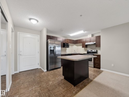 The property features a kitchen with dark cabinetry, stainless steel appliances, and a central island with a light-colored countertop - 1111 9363 Simpson Drive, Edmonton, AB - Indoor Photo Showing Kitchen With Upgraded Kitchen