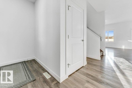 Entryway featuring light-toned flooring, a closed white door, and a staircase with a white railing - 1912 27 Street Nw, Edmonton, AB - Indoor Photo Showing Other Room