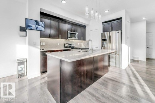 The kitchen features dark wood cabinetry, stainless steel appliances, a center island with a white countertop, and pendant lighting fixtures - 1912 27 Street Nw, Edmonton, AB - Indoor Photo Showing Kitchen With Stainless Steel Kitchen With Upgraded Kitchen