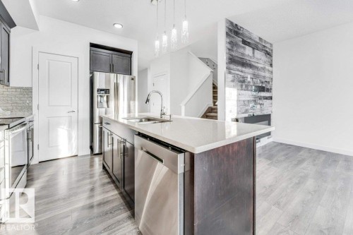 Open concept living space featuring a kitchen island with a sink, stainless steel appliances, light wood-style flooring, and a decorative accent wall - 1912 27 Street Nw, Edmonton, AB - Indoor Photo Showing Kitchen With Stainless Steel Kitchen With Double Sink With Upgraded Kitchen