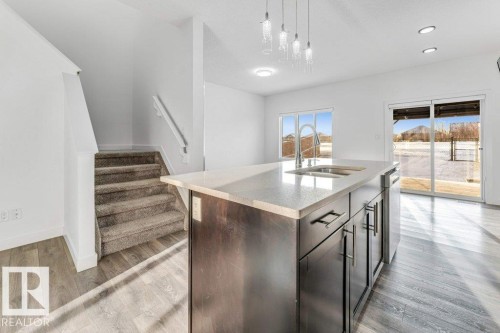 The property features an open-concept living space with light wood-style flooring, a kitchen island with a sink and ample cabinet space, and sliding glass doors leading to the exterior - 1912 27 Street Nw, Edmonton, AB - Indoor