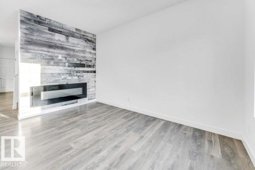 Living area featuring light-toned flooring, a fireplace with a dark grey accent wall, and white walls - 1912 27 Street Nw, Edmonton, AB - Indoor With Fireplace