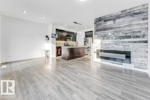 Open concept living space featuring light wood-style flooring, white walls, and a feature wall with horizontal wood paneling and a modern fireplace - 1912 27 Street Nw, Edmonton, AB - Indoor With Fireplace