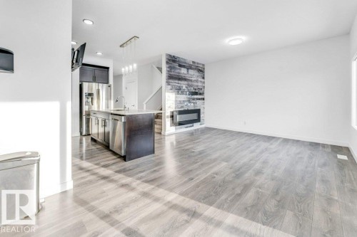 This inviting living space features light-toned flooring, a modern fireplace with a textured accent wall, and a window providing natural light - 1912 27 Street Nw, Edmonton, AB - Indoor With Fireplace