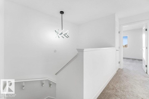 The property features a staircase with a white railing and a modern hanging light fixture - 1912 27 Street Nw, Edmonton, AB - Indoor Photo Showing Other Room