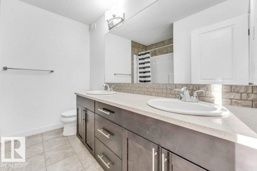 Bathroom featuring a dual vanity with a light-colored countertop, dark wood cabinetry, and a full-width mirror - 1912 27 Street Nw, Edmonton, AB - Indoor Photo Showing Bathroom