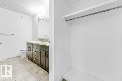 The property features a spacious closet with a hanging rod and shelving, alongside a bathroom with a dual vanity, tile flooring, and a toilet - 1912 27 Street Nw, Edmonton, AB - Indoor Photo Showing Bathroom