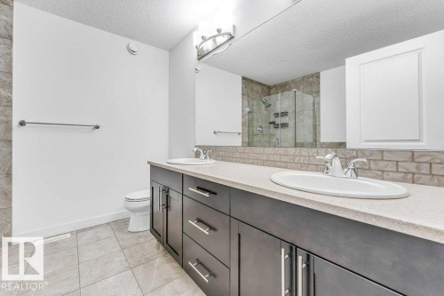 This bathroom features a double vanity with two sinks and dark cabinetry, a light-colored countertop, and a tiled backsplash - 1912 27 Street Nw, Edmonton, AB - Indoor Photo Showing Bathroom