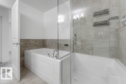Bathroom featuring a combination tub and shower with a glass enclosure, tiled walls, and sconce lighting - 1912 27 Street Nw, Edmonton, AB - Indoor Photo Showing Bathroom