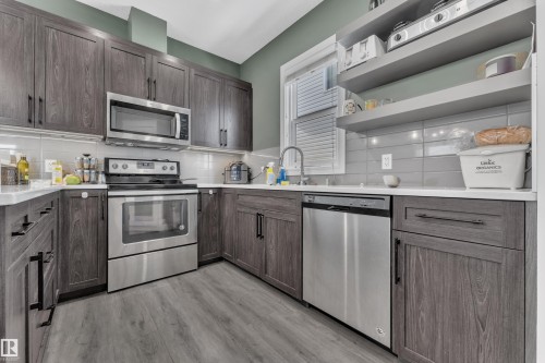The kitchen features dark wood-grain cabinetry, stainless steel appliances including a microwave, oven, and dishwasher, and light-colored countertops - 195 Kirpatrick Way, Leduc, AB - Indoor Photo Showing Kitchen With Stainless Steel Kitchen With Upgraded Kitchen
