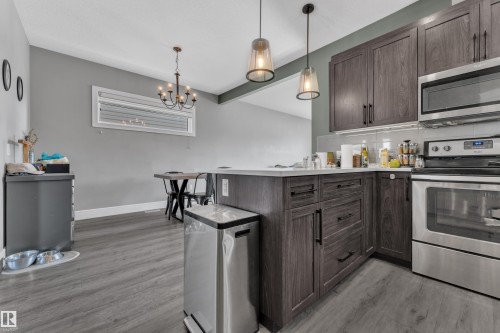 The kitchen features wood grain cabinetry with dark hardware, stainless steel appliances, and a light-colored countertop - 195 Kirpatrick Way, Leduc, AB - Indoor Photo Showing Kitchen With Stainless Steel Kitchen