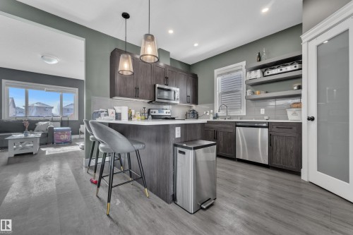 The kitchen features dark wood cabinetry, stainless steel appliances, and a central island with bar seating - 195 Kirpatrick Way, Leduc, AB - Indoor Photo Showing Kitchen With Stainless Steel Kitchen With Upgraded Kitchen