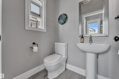 Bathroom featuring a pedestal sink, a toilet, a window, and a wall mirror with a metallic frame - 195 Kirpatrick Way, Leduc, AB - Indoor Photo Showing Bathroom