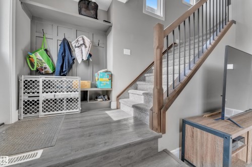 Entryway featuring a built-in bench with storage cubbies and wall hooks, alongside a staircase with carpeted treads and a wooden handrail with black metal balusters - 195 Kirpatrick Way, Leduc, AB - Indoor Photo Showing Other Room
