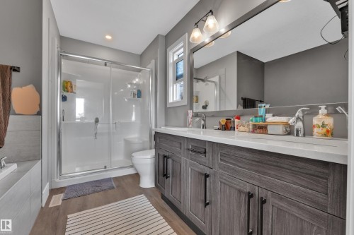 Bathroom featuring a double vanity with a light-colored countertop and dark wood cabinetry, a large mirror, and a walk-in shower with a glass enclosure - 195 Kirpatrick Way, Leduc, AB - Indoor Photo Showing Bathroom