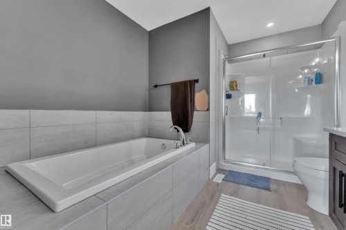 The bathroom features a built-in bathtub with light grey tiling, a shower with a sliding glass door, and light wood-style flooring - 195 Kirpatrick Way, Leduc, AB - Indoor Photo Showing Bathroom