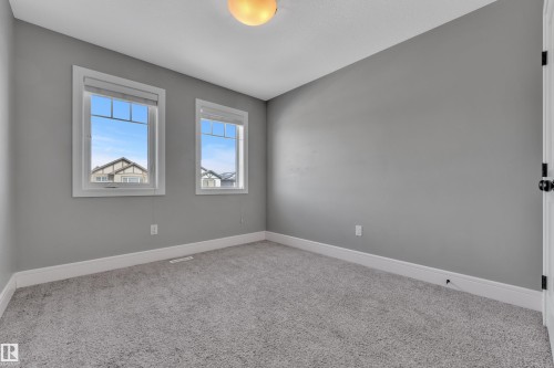 This room features neutral grey walls, light grey carpet, and two windows providing natural illumination - 195 Kirpatrick Way, Leduc, AB - Indoor Photo Showing Other Room