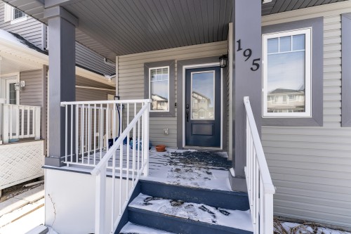 The property features a front porch with white railings, grey siding, and a dark blue front door - 195 Kirpatrick Way, Leduc, AB - Outdoor With Exterior