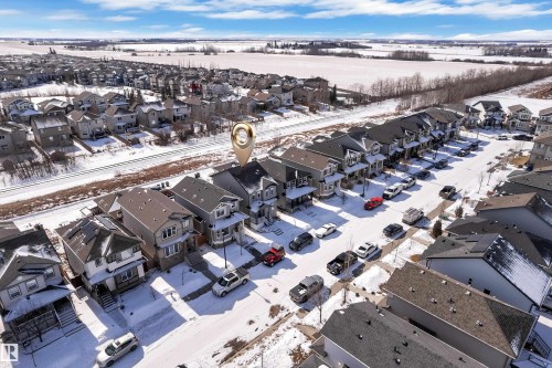 Aerial view of the property and its surrounding neighborhood, featuring residential properties with pitched roofs, a street with parked vehicles, and a clear blue sky - 195 Kirpatrick Way, Leduc, AB - Outdoor With View