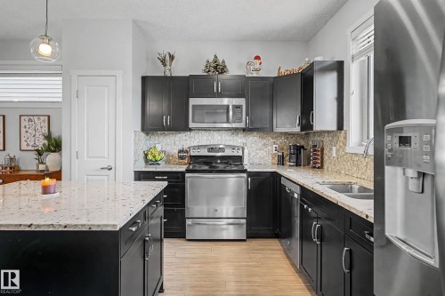 Kitchen featuring dark cabinets, stainless steel appliances, light stone counters, tasteful backsplash, and pendant lighting - 4110 Allan Crescent, Edmonton, AB - Indoor Photo Showing Kitchen With Double Sink With Upgraded Kitchen