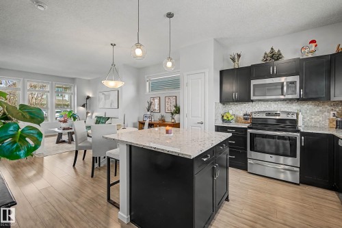 Kitchen with dark cabinetry, stainless steel appliances, light stone counters, and a textured ceiling - 4110 Allan Crescent, Edmonton, AB - Indoor Photo Showing Kitchen With Upgraded Kitchen