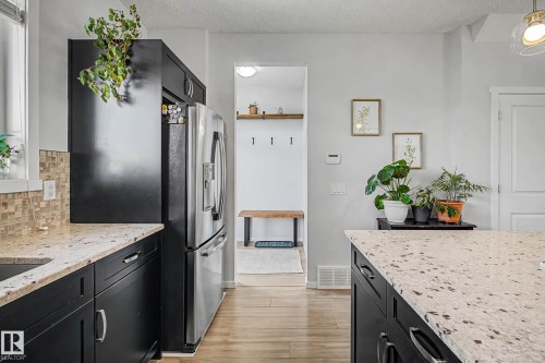Kitchen with dark cabinets, light stone counters, stainless steel fridge, a textured ceiling, and light wood-style floors - 4110 Allan Crescent, Edmonton, AB - Indoor Photo Showing Kitchen With Upgraded Kitchen