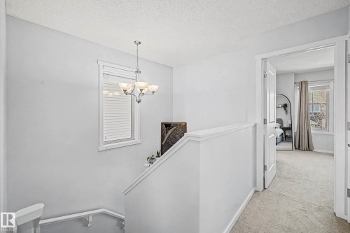 Hall featuring a textured ceiling, light carpet, hanging lights, and an upstairs landing - 4110 Allan Crescent, Edmonton, AB - Indoor Photo Showing Other Room
