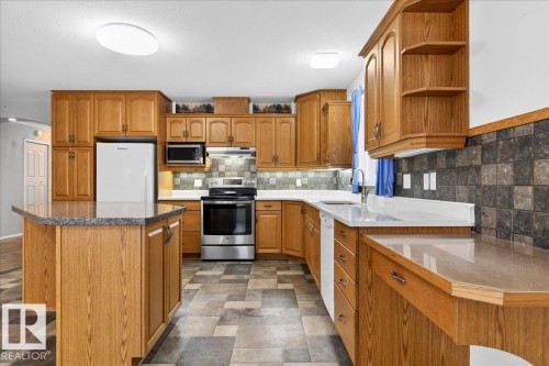 The kitchen features wood cabinetry, a central island with a countertop, stainless steel appliances including a refrigerator, oven, and microwave, and a tile backsplash - 4412 Yeoman Close, Onoway, AB - Indoor Photo Showing Kitchen With Double Sink