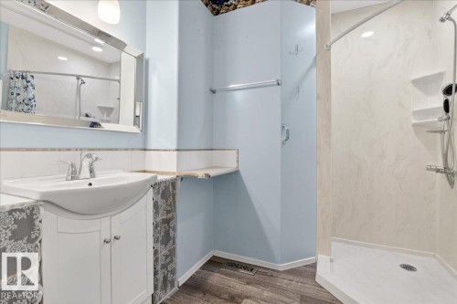 This bathroom features a vanity with a white sink and chrome faucet, a wall-mounted mirror, and a walk-in shower with shelving - 4412 Yeoman Close, Onoway, AB - Indoor Photo Showing Bathroom