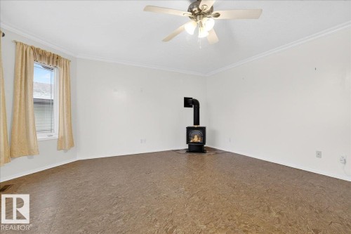 This room features a window with blinds and curtains, a ceiling fan with integrated lighting, and a freestanding fireplace - 4412 Yeoman Close, Onoway, AB - Indoor Photo Showing Other Room
