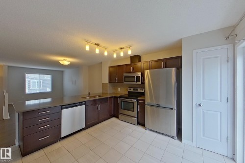The kitchen features dark wood cabinetry, stainless steel appliances, and a tiled floor - 87 4050 Savaryn Drive, Edmonton, AB - Indoor Photo Showing Kitchen