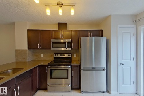 The kitchen features stainless steel appliances, including a refrigerator, oven, and microwave - 87 4050 Savaryn Drive, Edmonton, AB - Indoor Photo Showing Kitchen