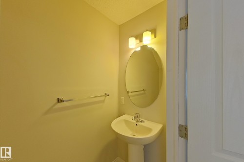 This space features a pedestal sink, an oval mirror with overhead lighting, and a wall-mounted towel bar - 87 4050 Savaryn Drive, Edmonton, AB - Indoor Photo Showing Bathroom